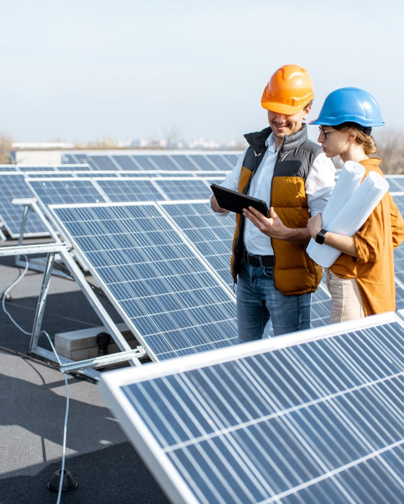 Two engineers or architects examining the construction of a solar power plant, walking with digital tablet on a rooftop